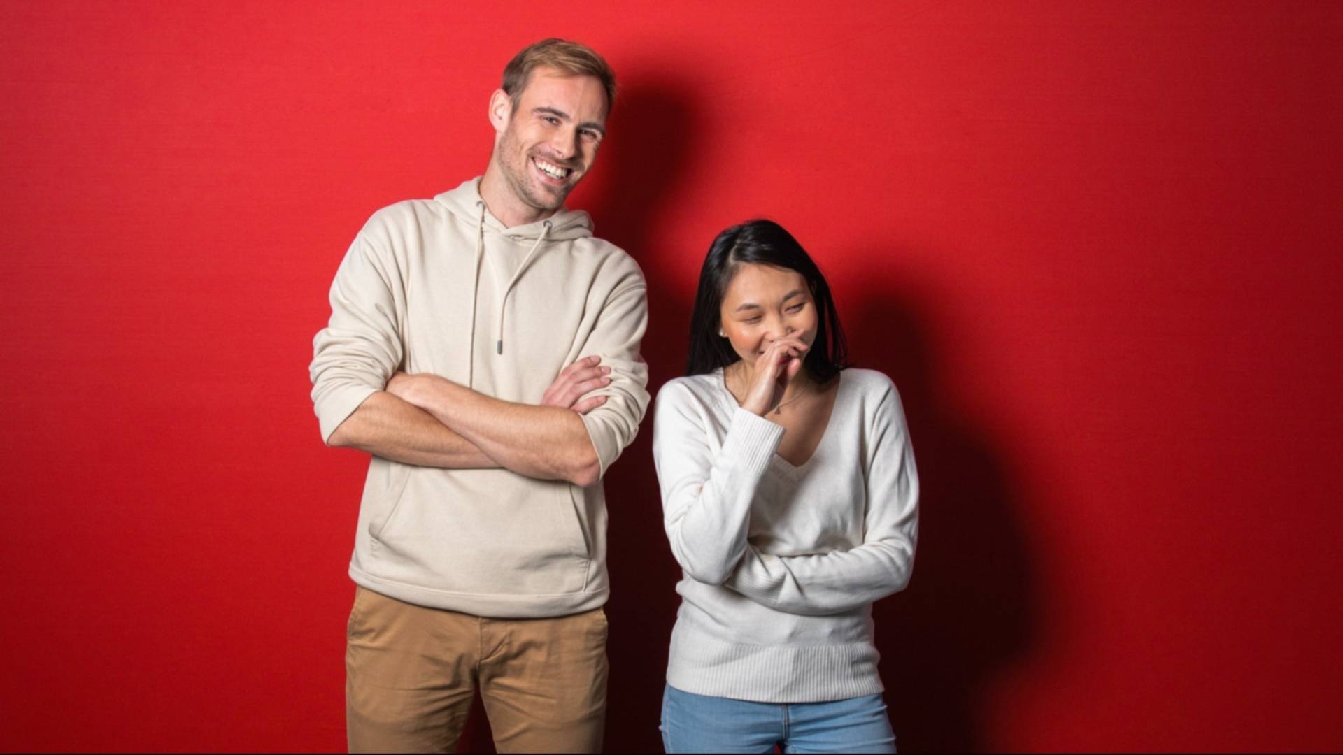 Portrait de deux jeunes collaborateurs en pull blanc, fond rouge