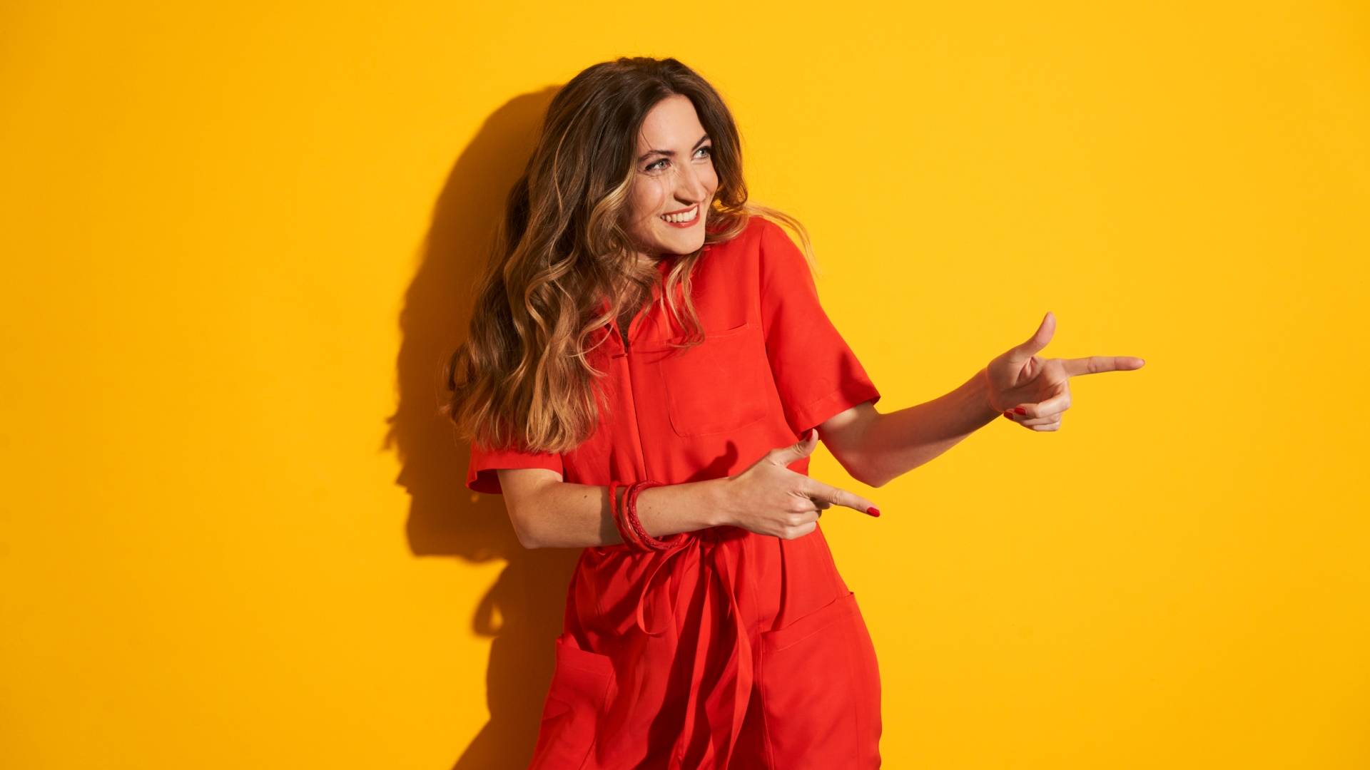 Une jeune femme souriante en robe rouge, fond jaune