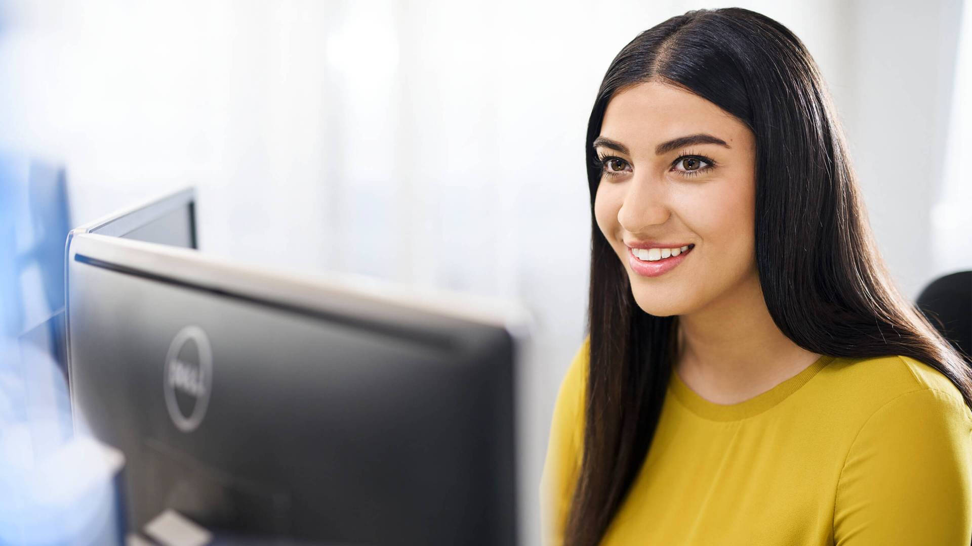 Un jeune femme souriante assise devant son poste de travail