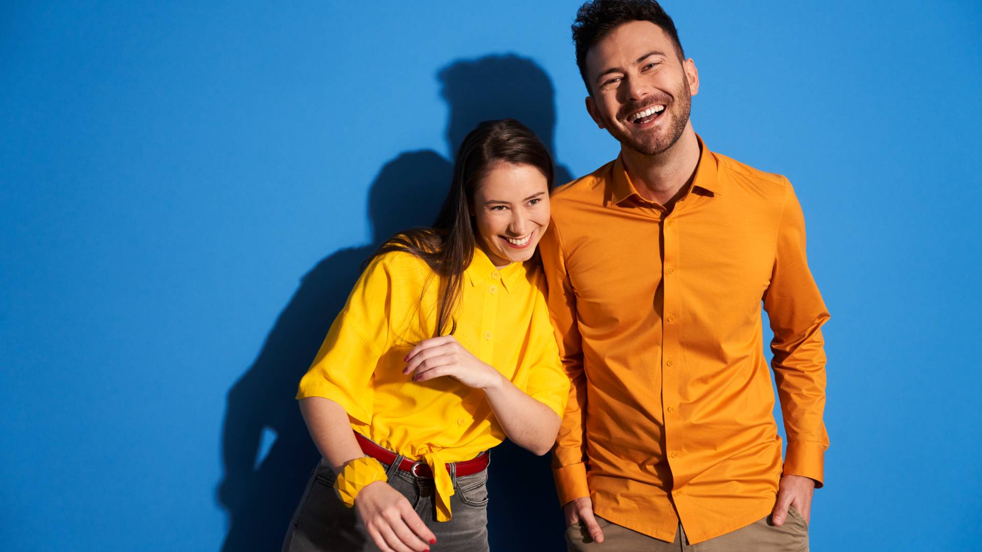 Portrait de deux jeunes souriants en chemise jaune, fond bleu