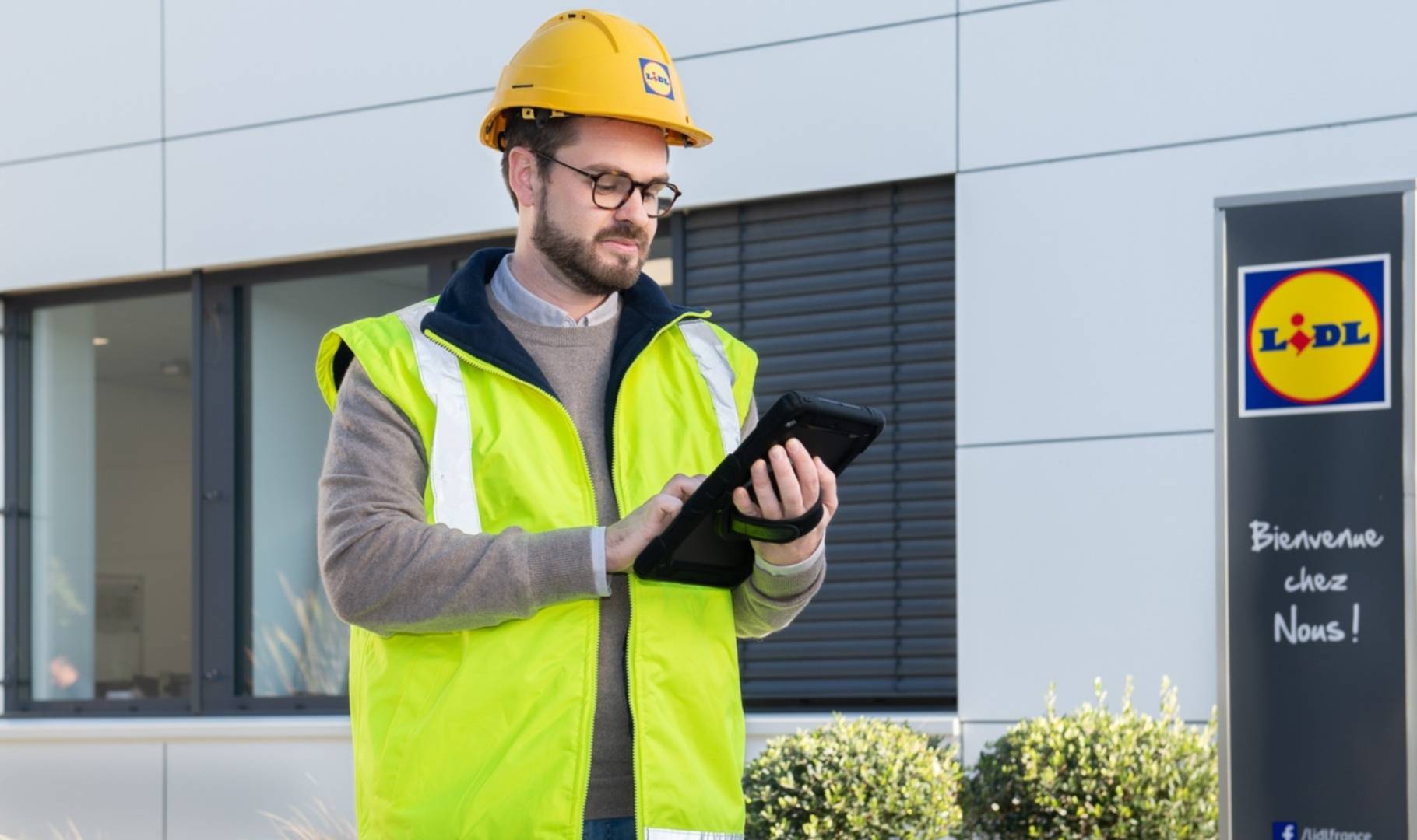 Homme avec un gilet de sécurité et casque de chantier, en train de vérifier des informations sur une tablette