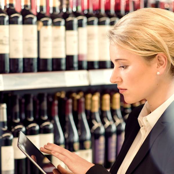 Une jeune femme en Supermarché avec une tablette à la main, devant le rayon Vins