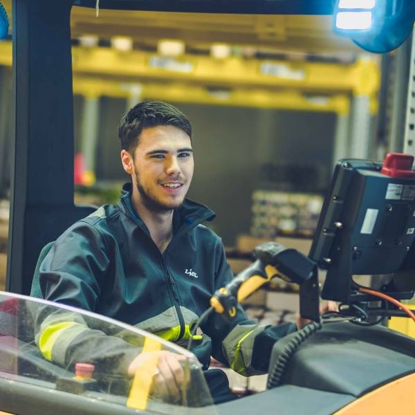 Un jeune employé conduit un chariot élévateur frontal dans une plateforme logistique