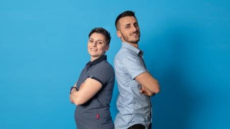 Deux employés de supermarché, en tenue de travail, se tiennent dos à dos et sourient à la caméra