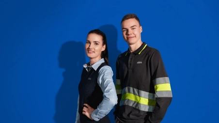 Deux employés de supermarché, en tenue de travail, se tiennent dos à dos et sourient à la caméra